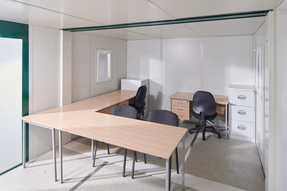 Interior of linked flat pack office cabin with two desks and filing cabinet